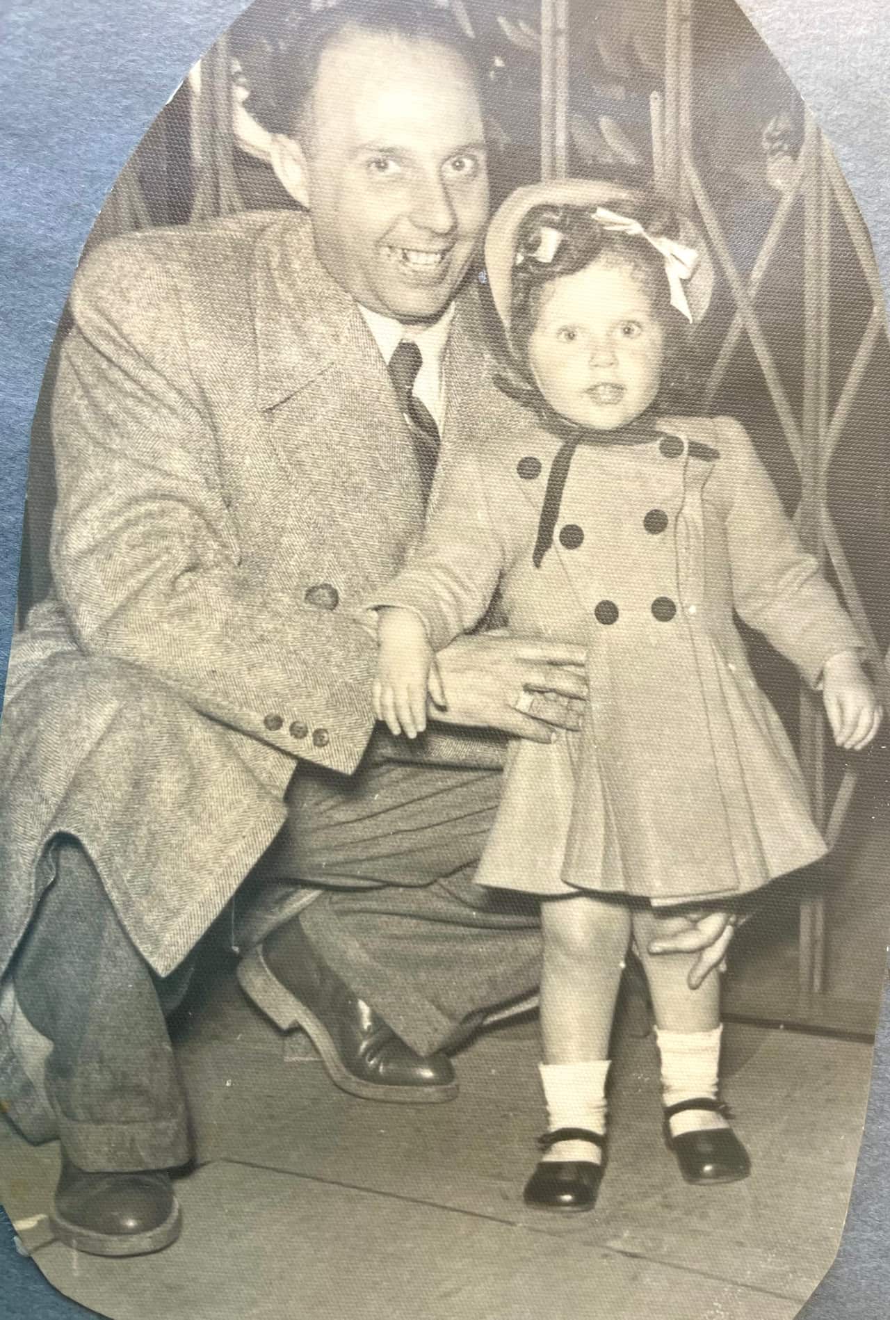 Black and white picture of a man in a jacket crouching down to hold a small female child.