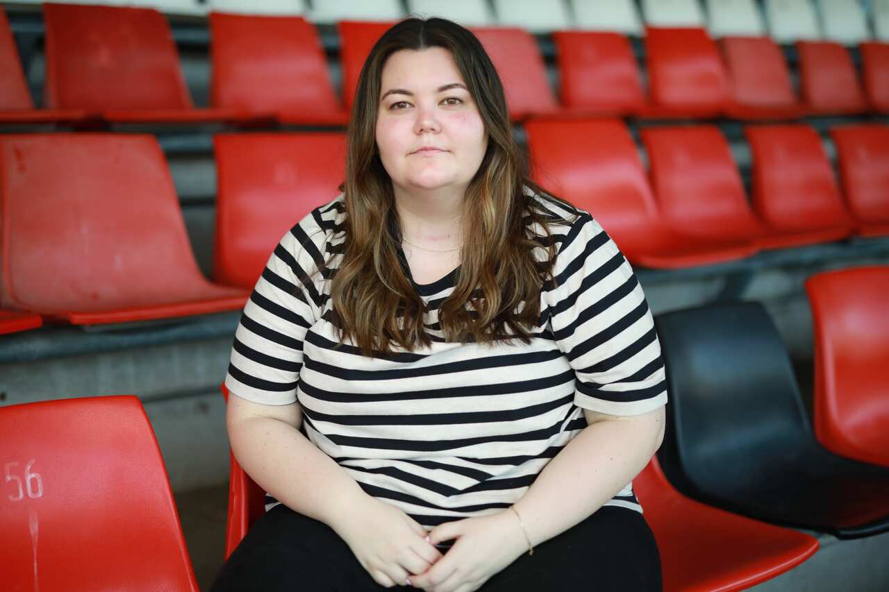 A woman sits in a football stadium stand. 