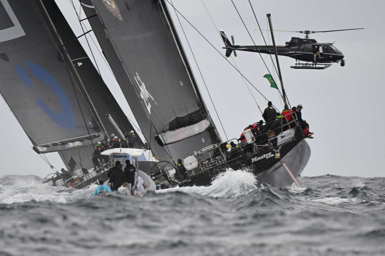 Yacht tipping sideways in choppy water, with a helicopter flying overhead.