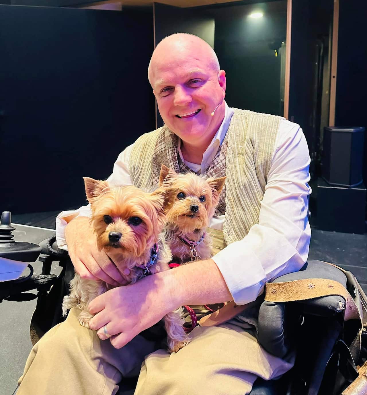 A man in a wheelchair, with two small dogs sitting on his lap.