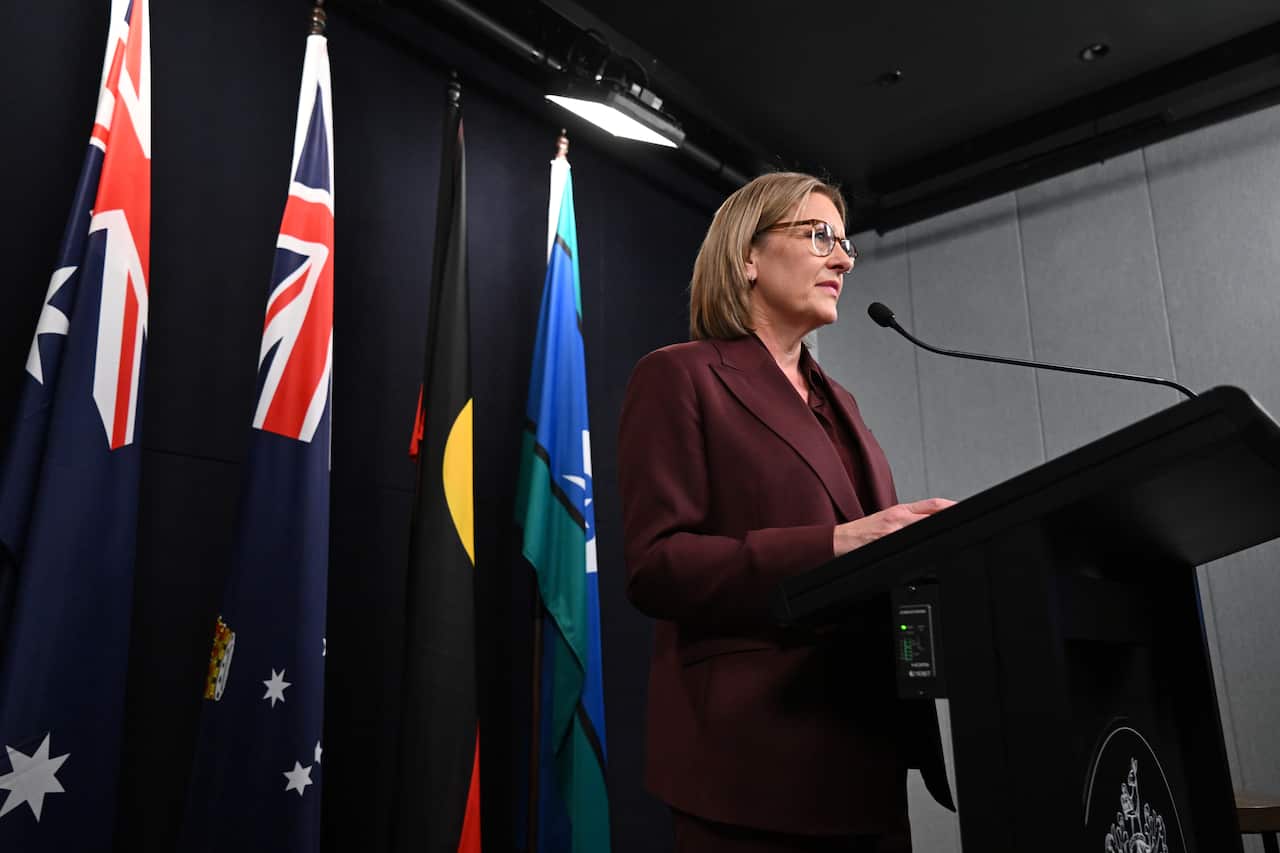 A middle aged white woman in a maroon suit standing at a podium