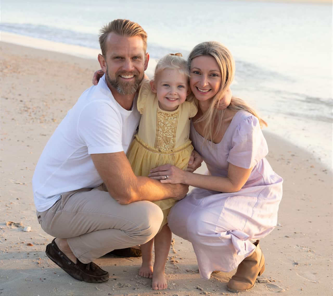 A man crouches on a beach with his arms around a woman and a child.