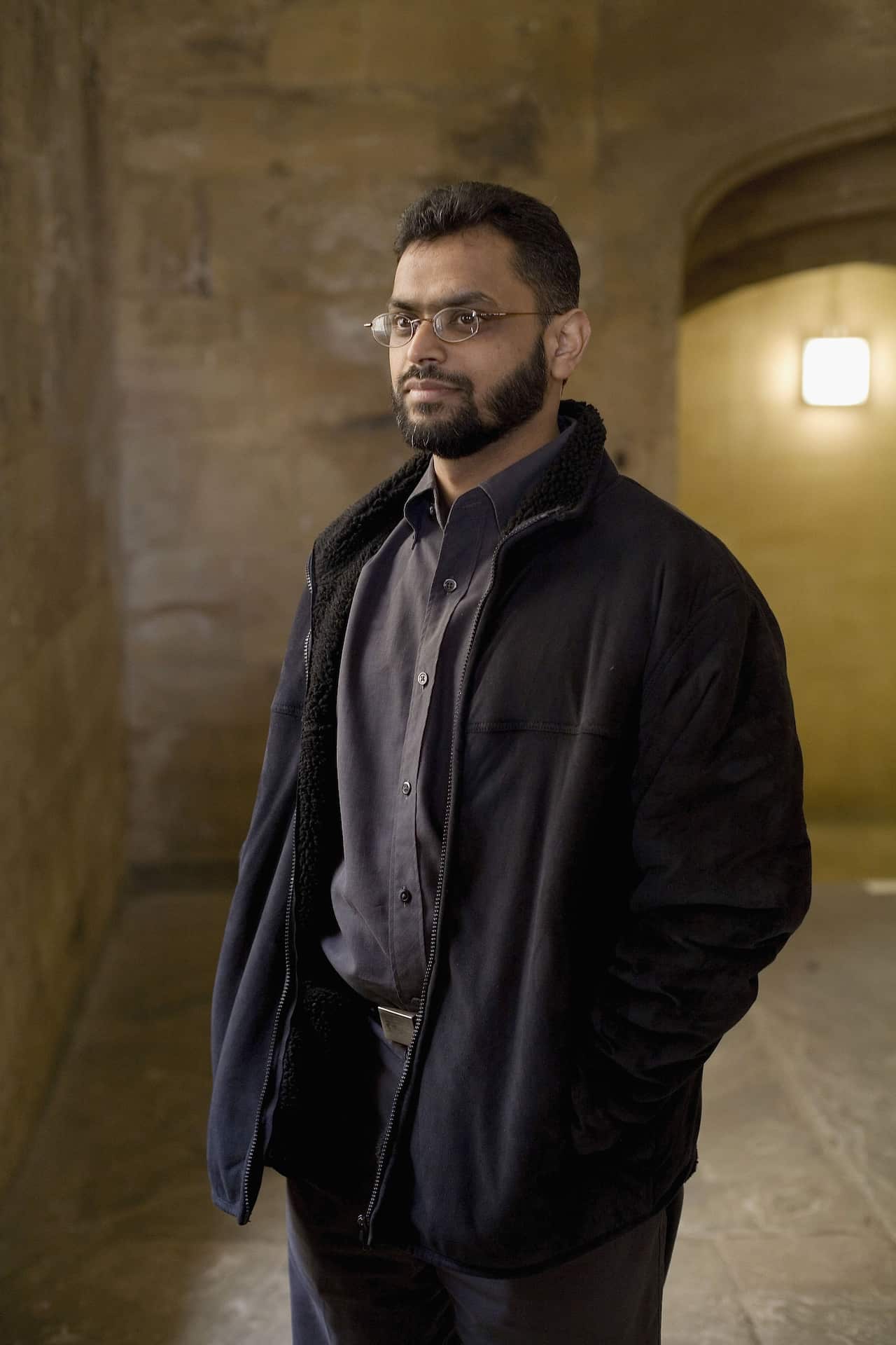 A man with a beard and glasses looks solemnly to the left as they are posing for a portrait photo