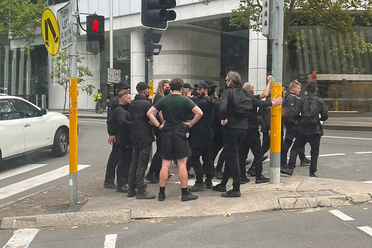 A group of men in the black clothes is crossing the road at the traffic light