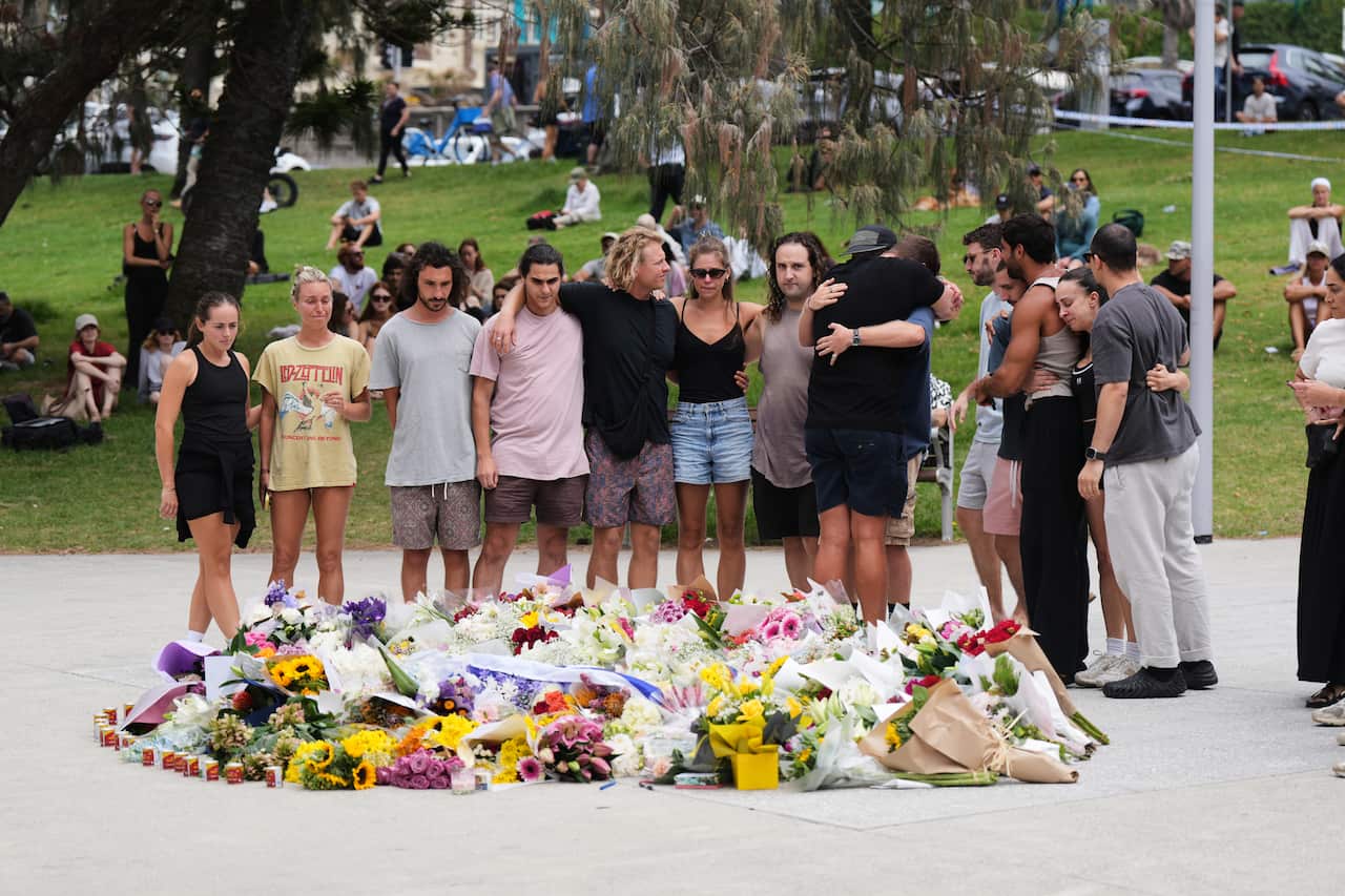 A group of young people standing close together in front of flowers placed on the ground.