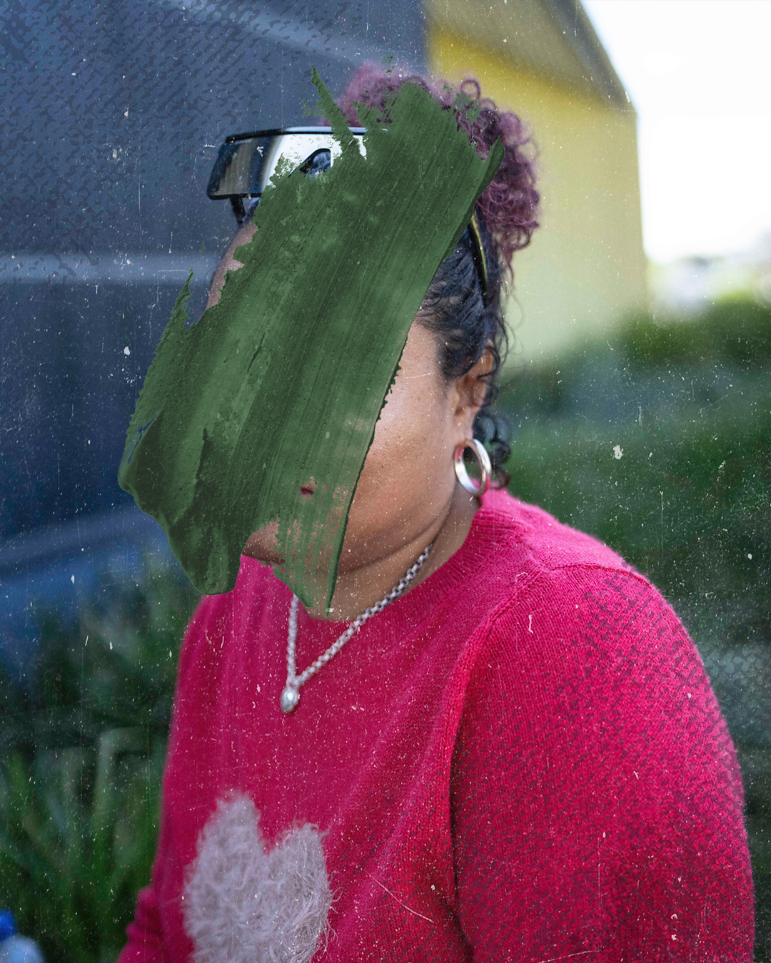 A woman with curly red hair wears a bright pink jumper with a white love heart on it. Her face is obscured by a black smudge.