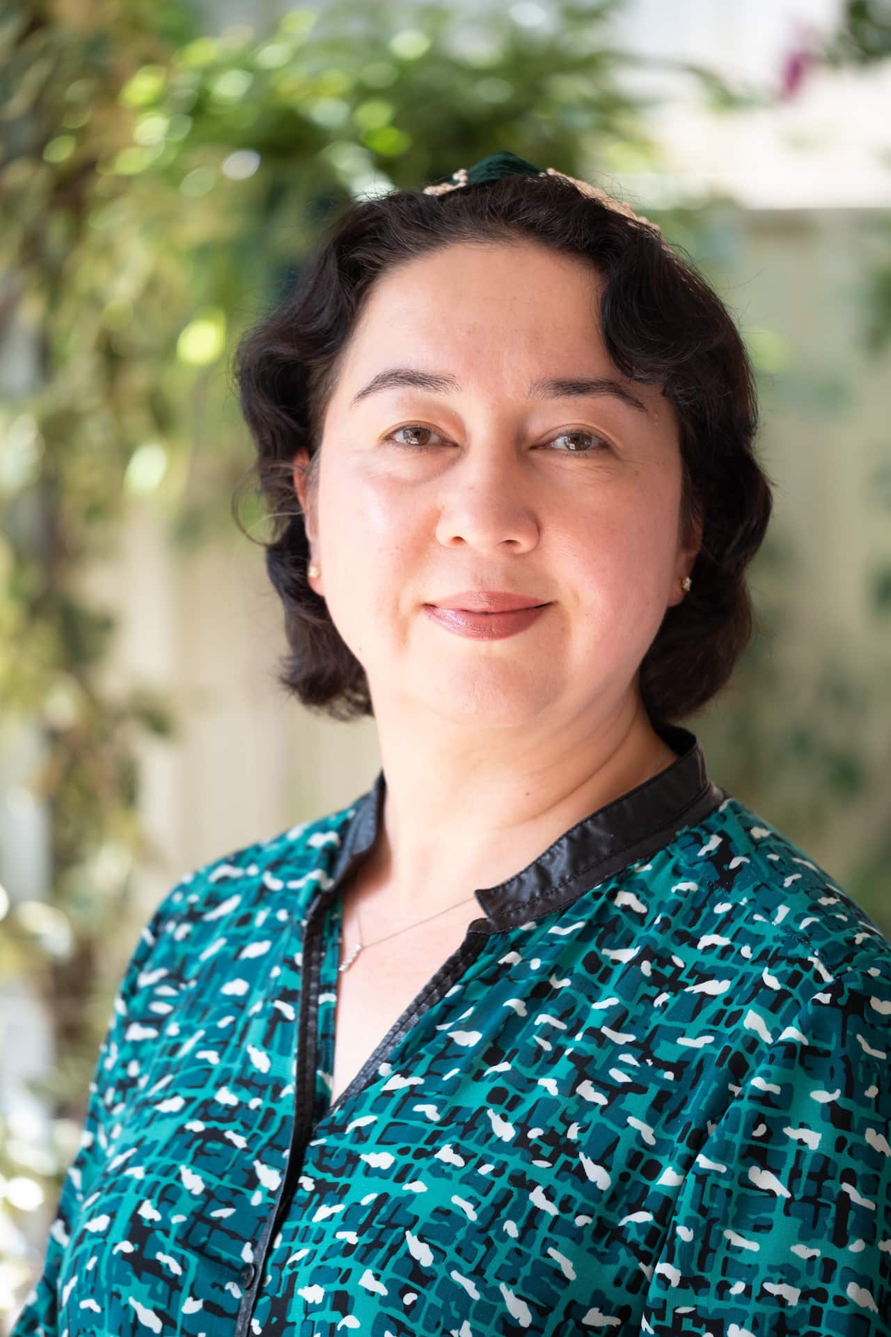 Headshot of Ramila smiling faintly in a green and black blouse.
