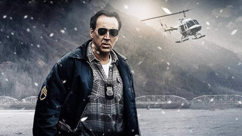 A policeman stands in the snow with his sunglasses on as a helicopter circles behind him