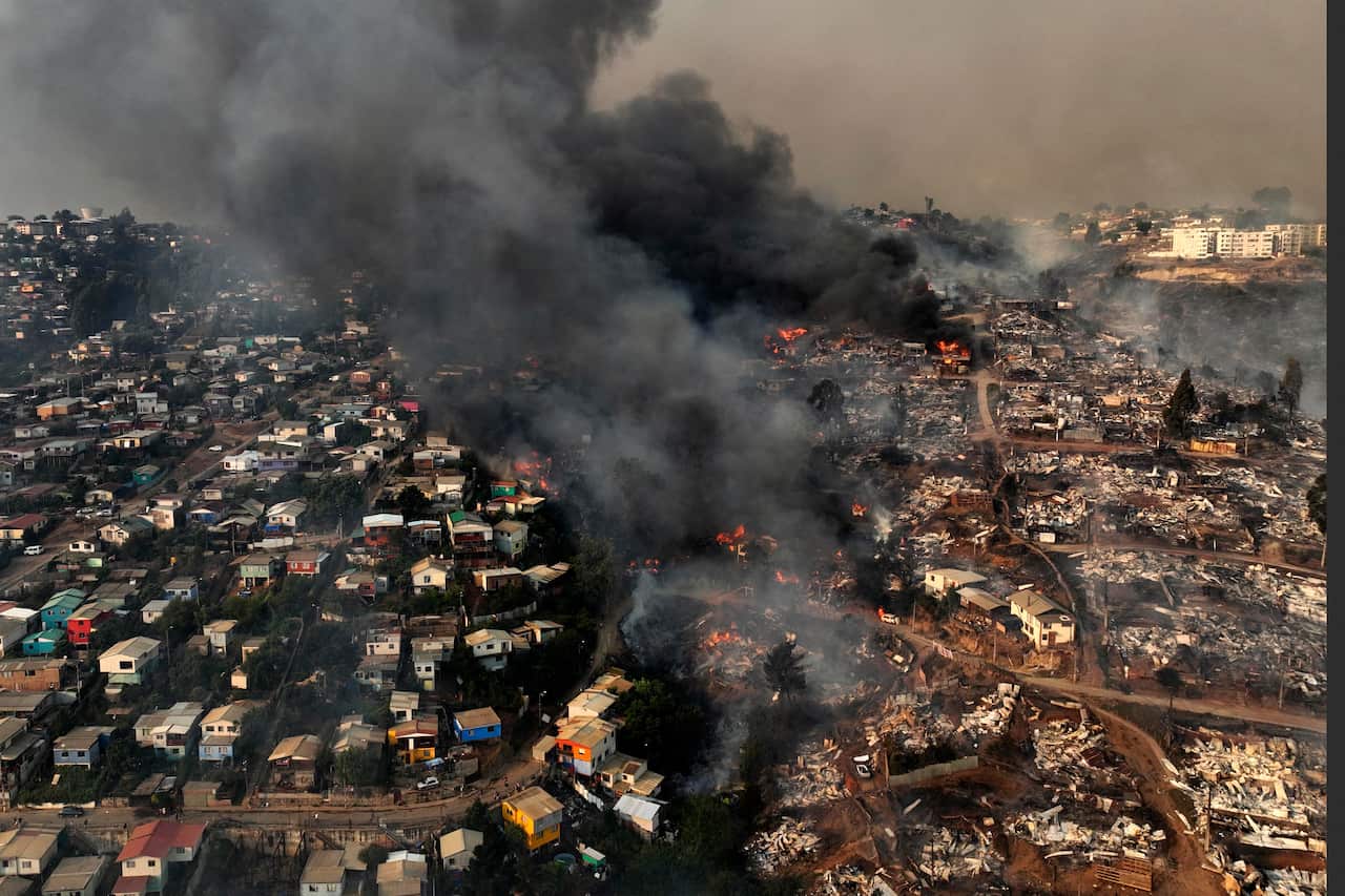 An aerial shot of a town, with a fire and smoke in the middle. One half of the town looks totally destroyed by fire. 