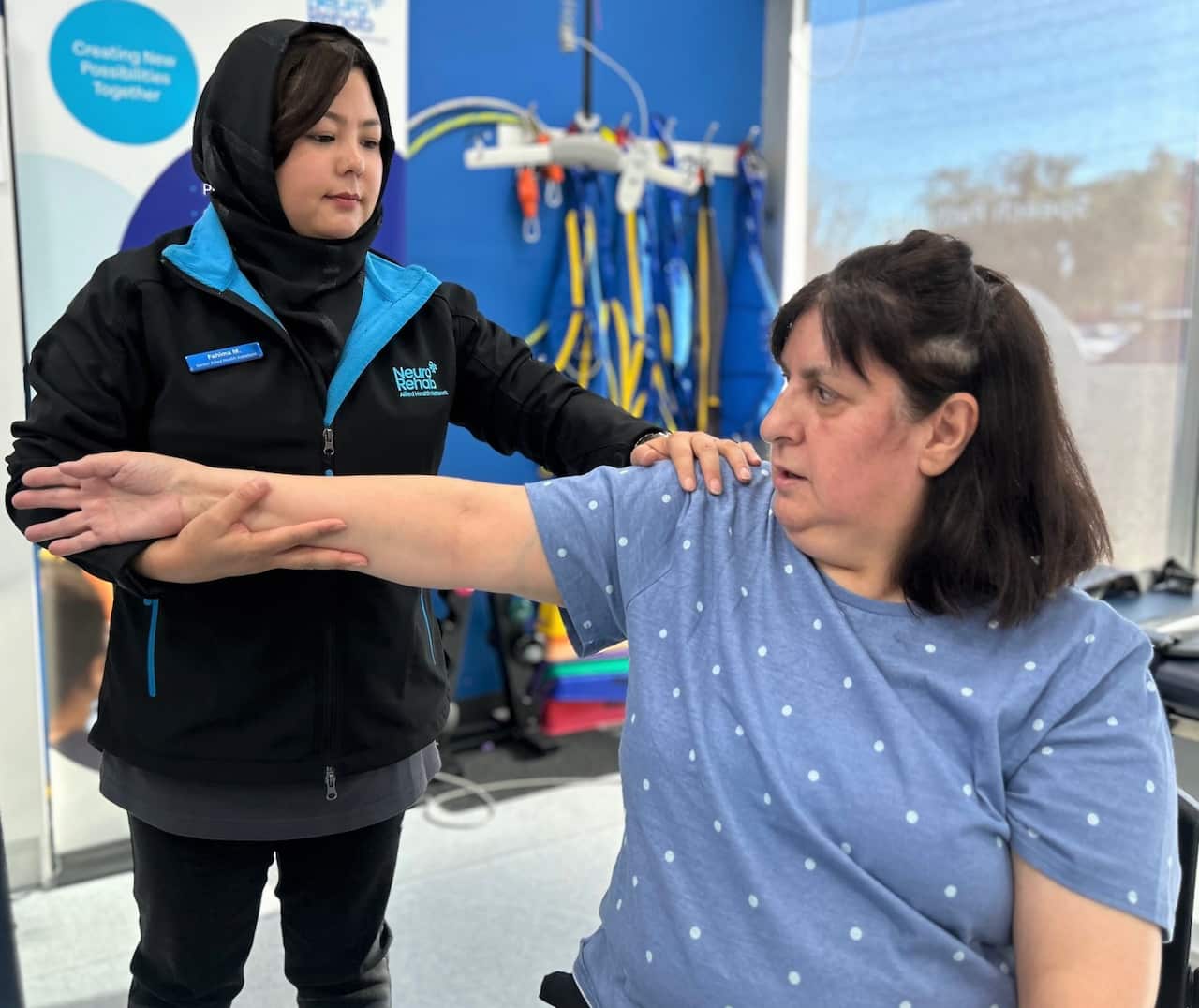 A woman in a blue and black jacket stands holding the arm of another woman in a blue T-shirt.