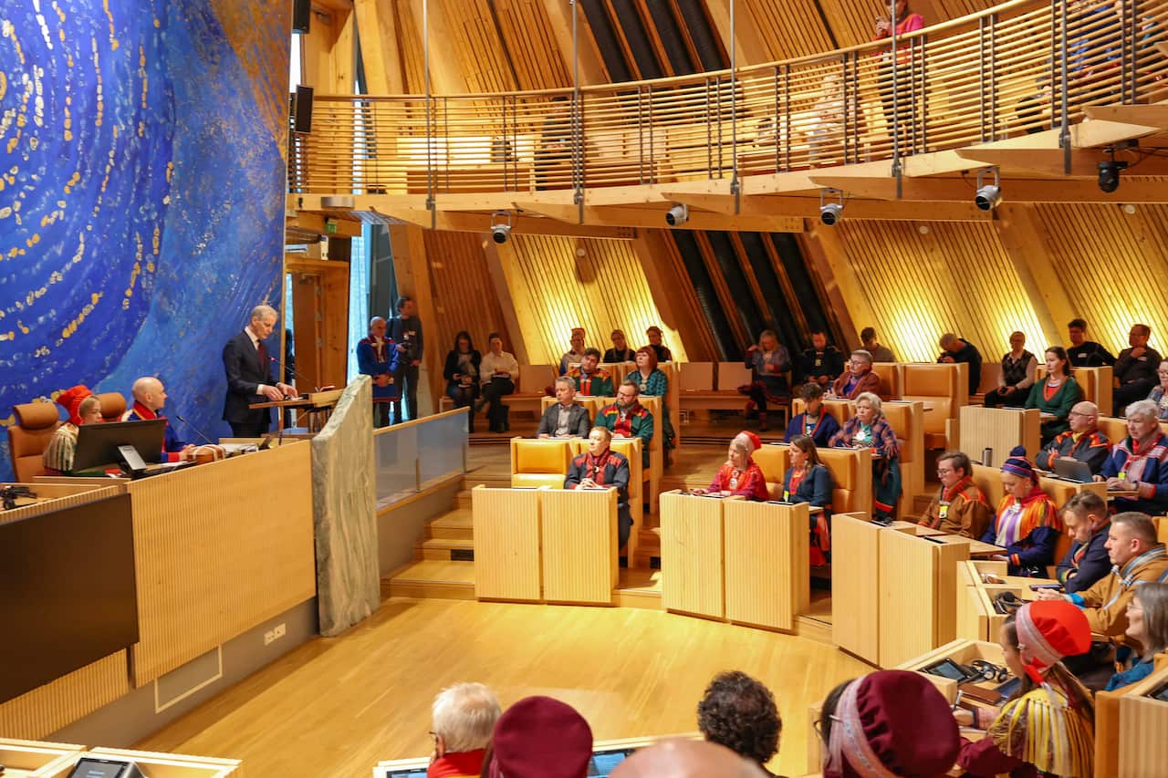 Man in suit addresses a chamber filled with people dressed in traditional Sami clothing.