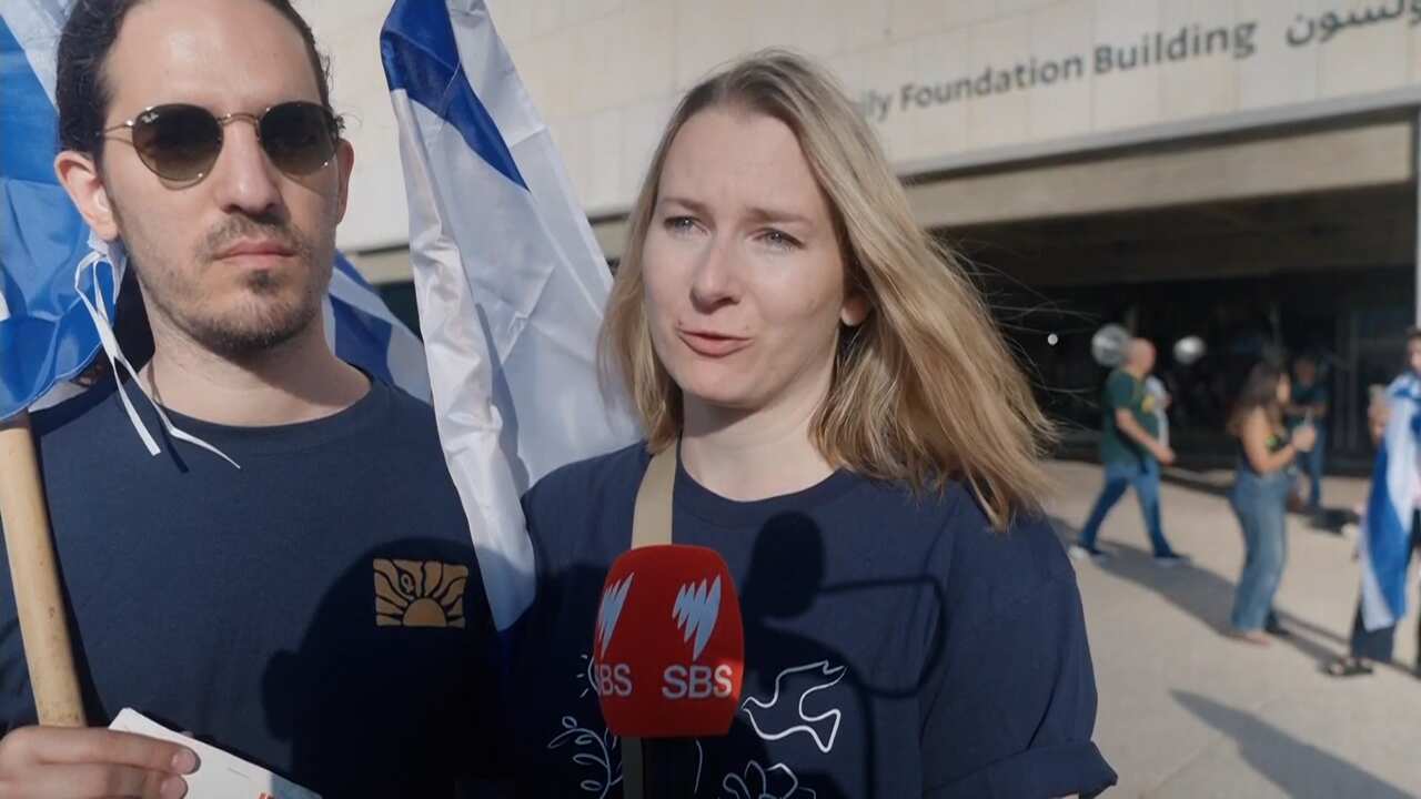 A man in sunglasses stands next to a woman speaking into a microphone