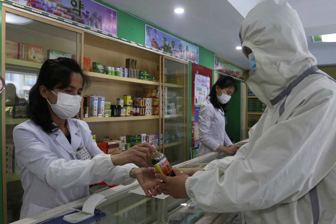 A pharmacy employee hands a bottle to a man who is wearing personal protective gear. 