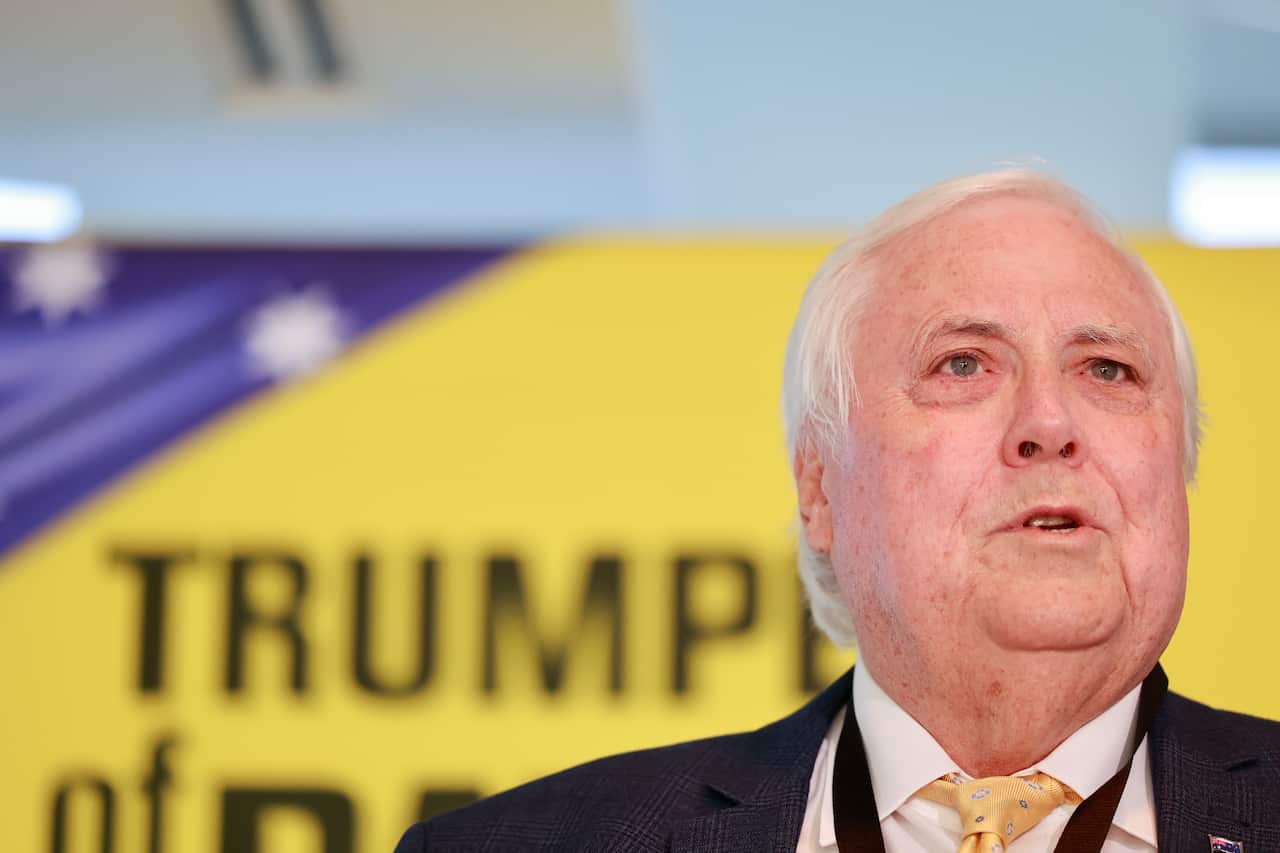A close up of Clive Palmer wearing a suit speaking, with a Trumpet of Patriots sign in the background