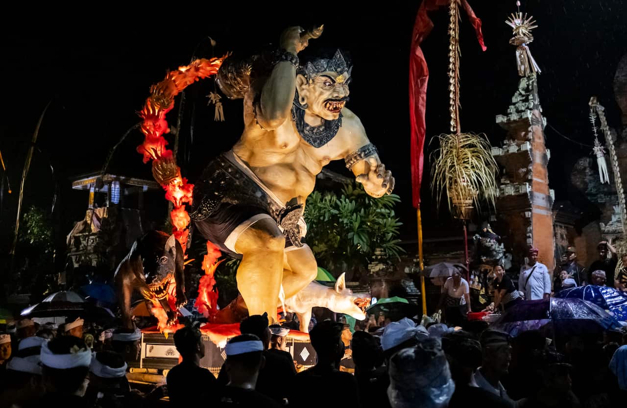 A larger-than-life Indonesian devil-like figure ebing observed by a crowd