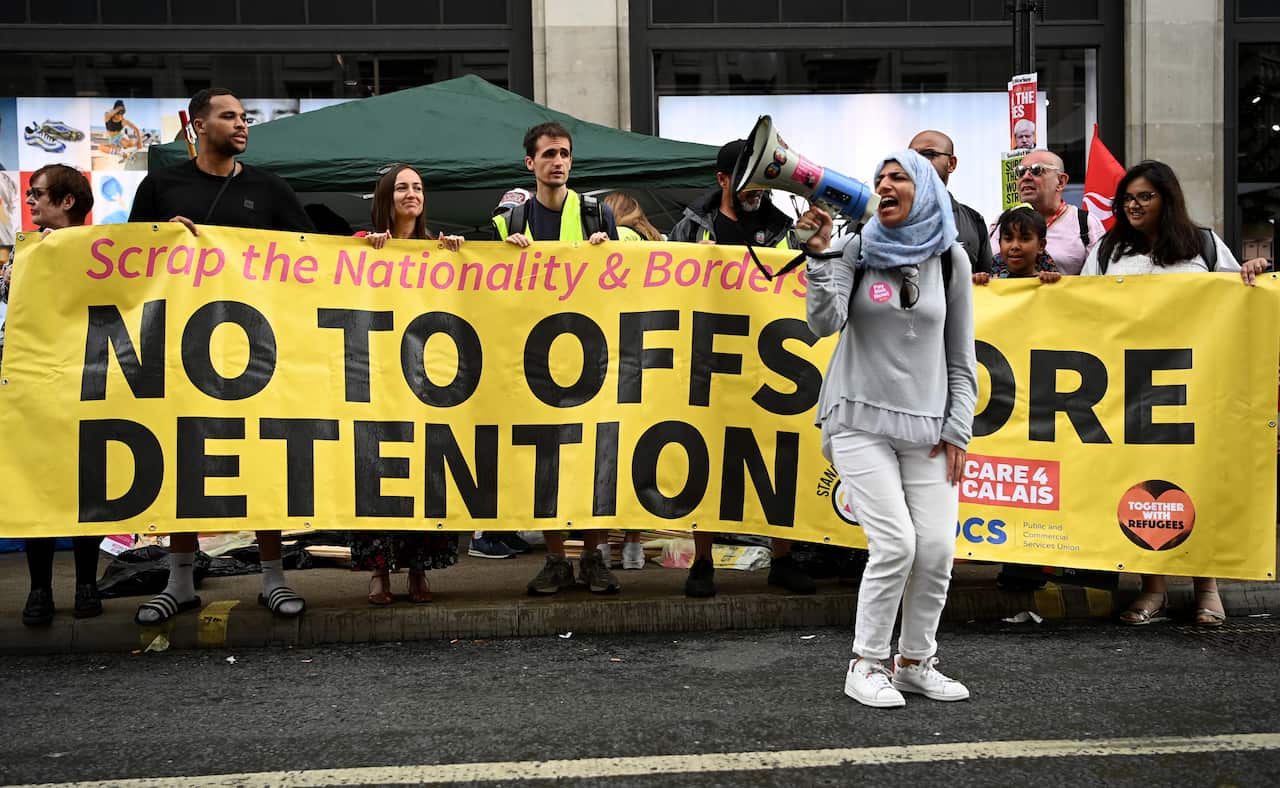 A woman with a head scarf shouts into a megaphone in front of a banner reading "no to offshore detention"