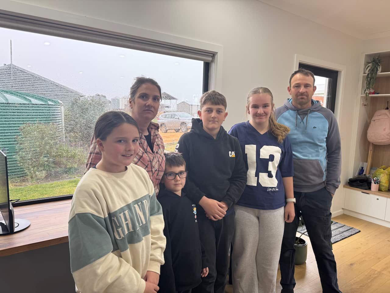 A family of six standing in front of a window looking concerned.