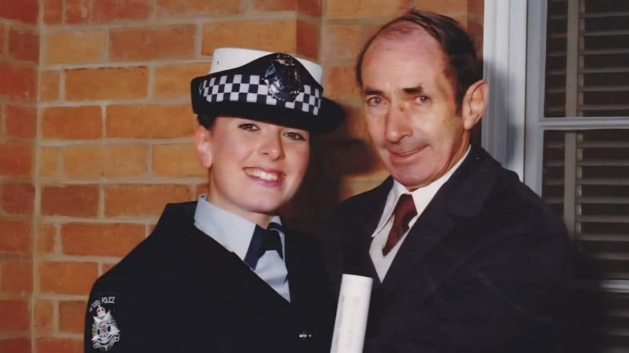 a photo of a young female police officer in uniform smiles with an older man in front of a brick wall