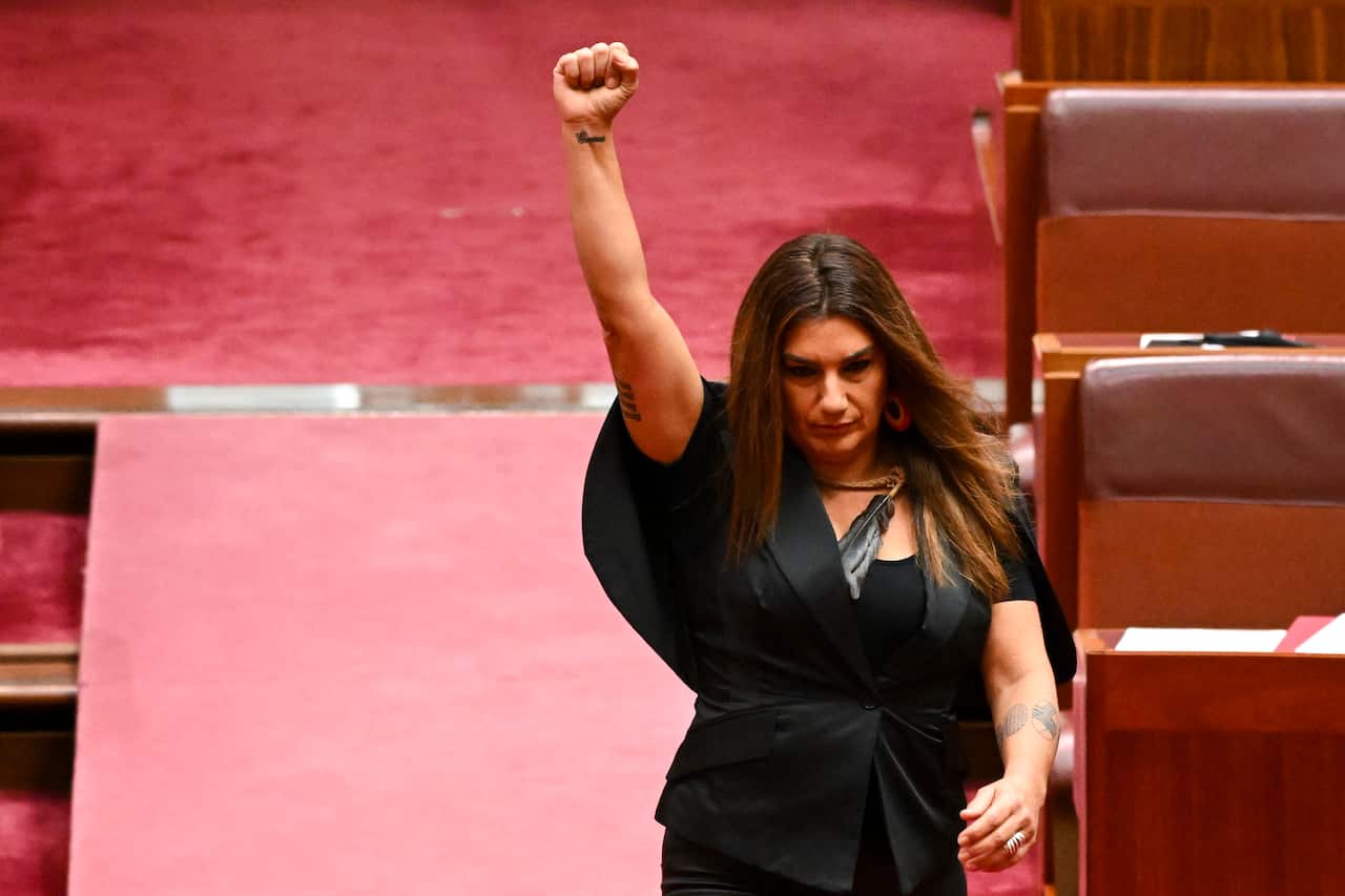 Woman in black short-sleeved black blazer raises her arm in the Senate chamber. 