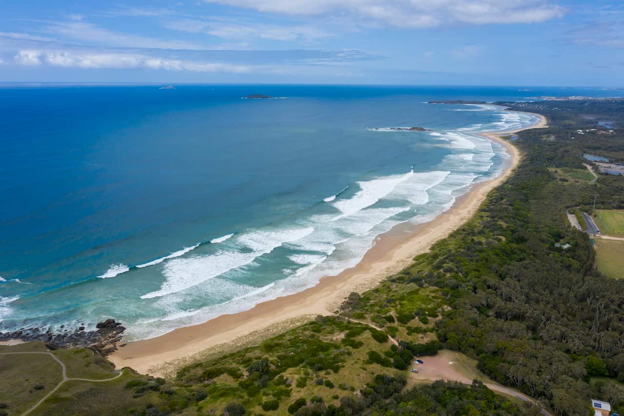An overhead shot of a long stretch of coastline with waves breaking.