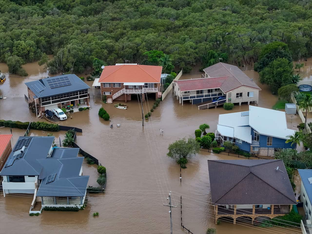 An aerial shot of houses submerged in brown floodwater.