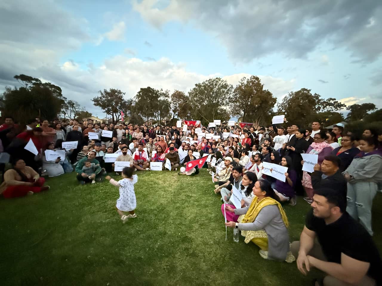 People holding signs stand in a circle in a park.
