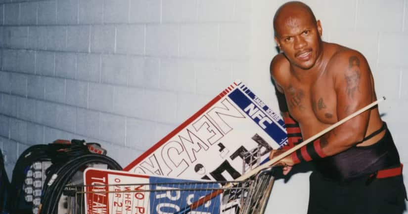 A man wearing wrestling gear and pushing a shopping cart.