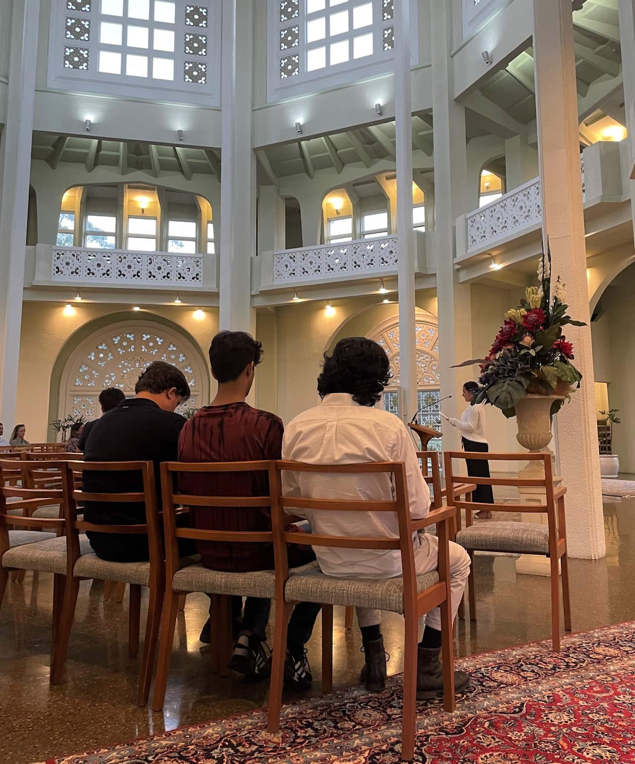 Men with their backs to camera sitting on chairs inside a Baha'i temple.