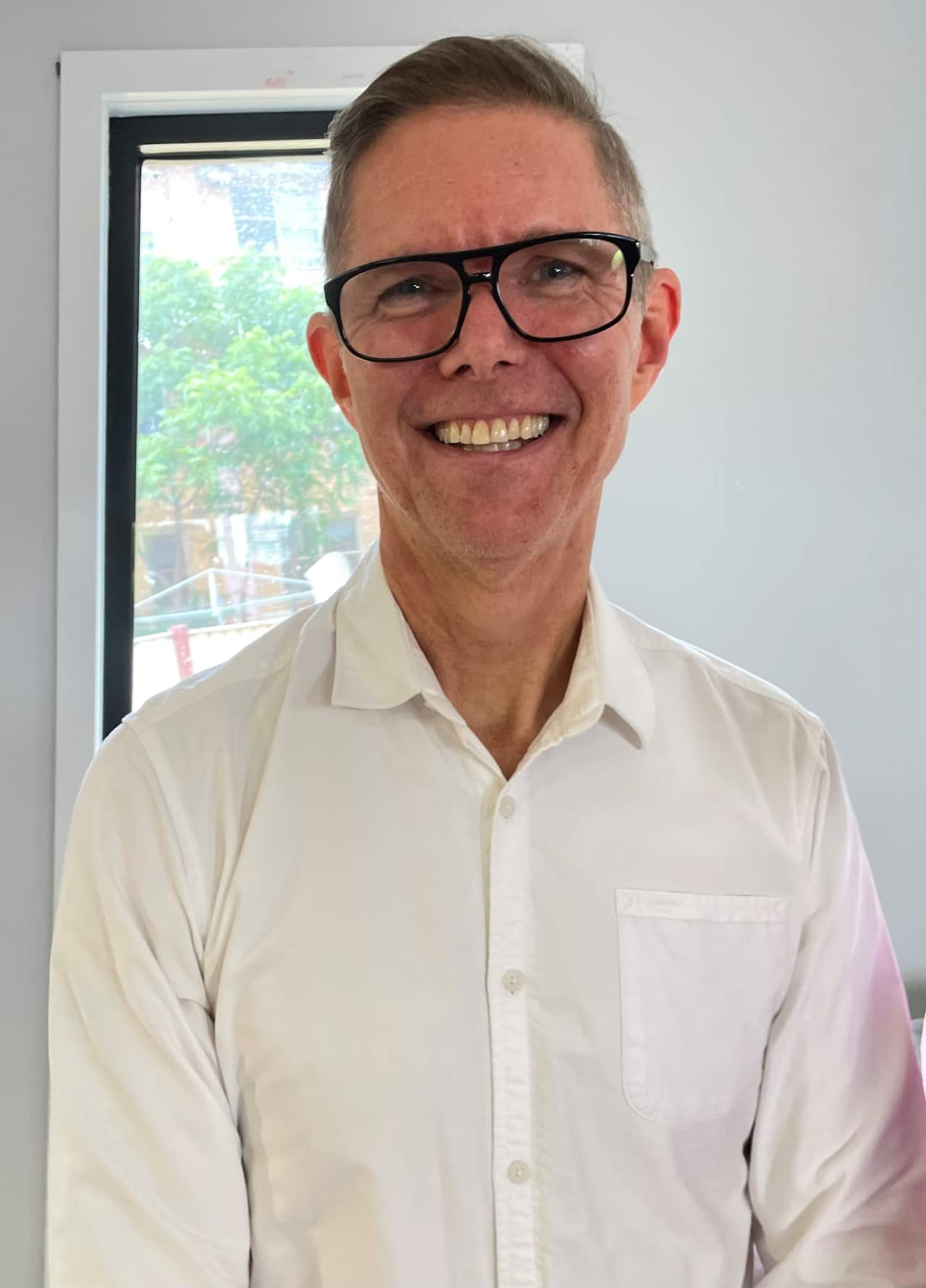 A man wearing glasses and a white shirt smiles at camera.
