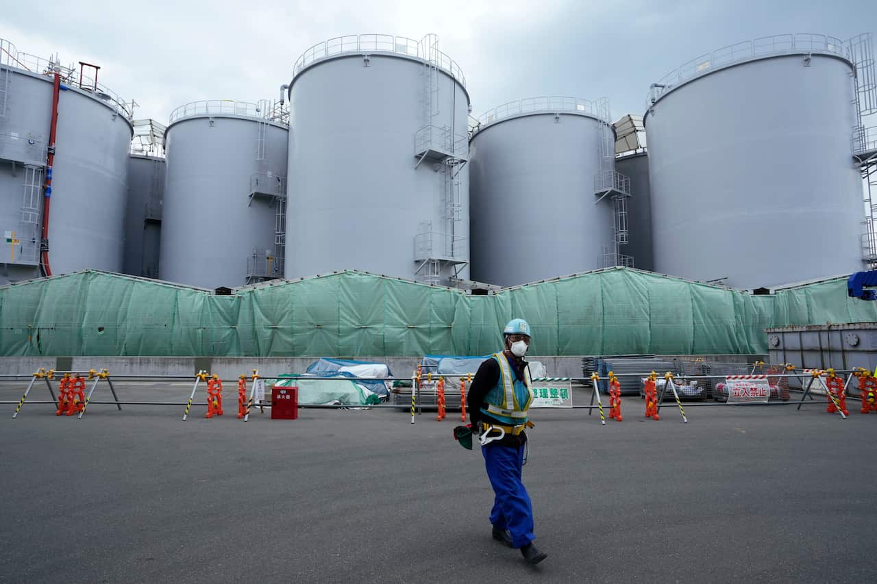 A man in a hard hat and face mask stands in front of giant tanks at a nuclear power plant.