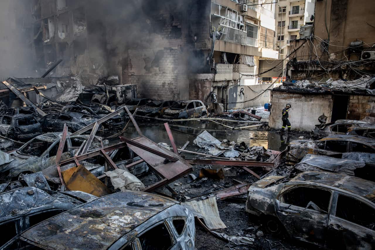 A firefighter walking past several burned-out cars.