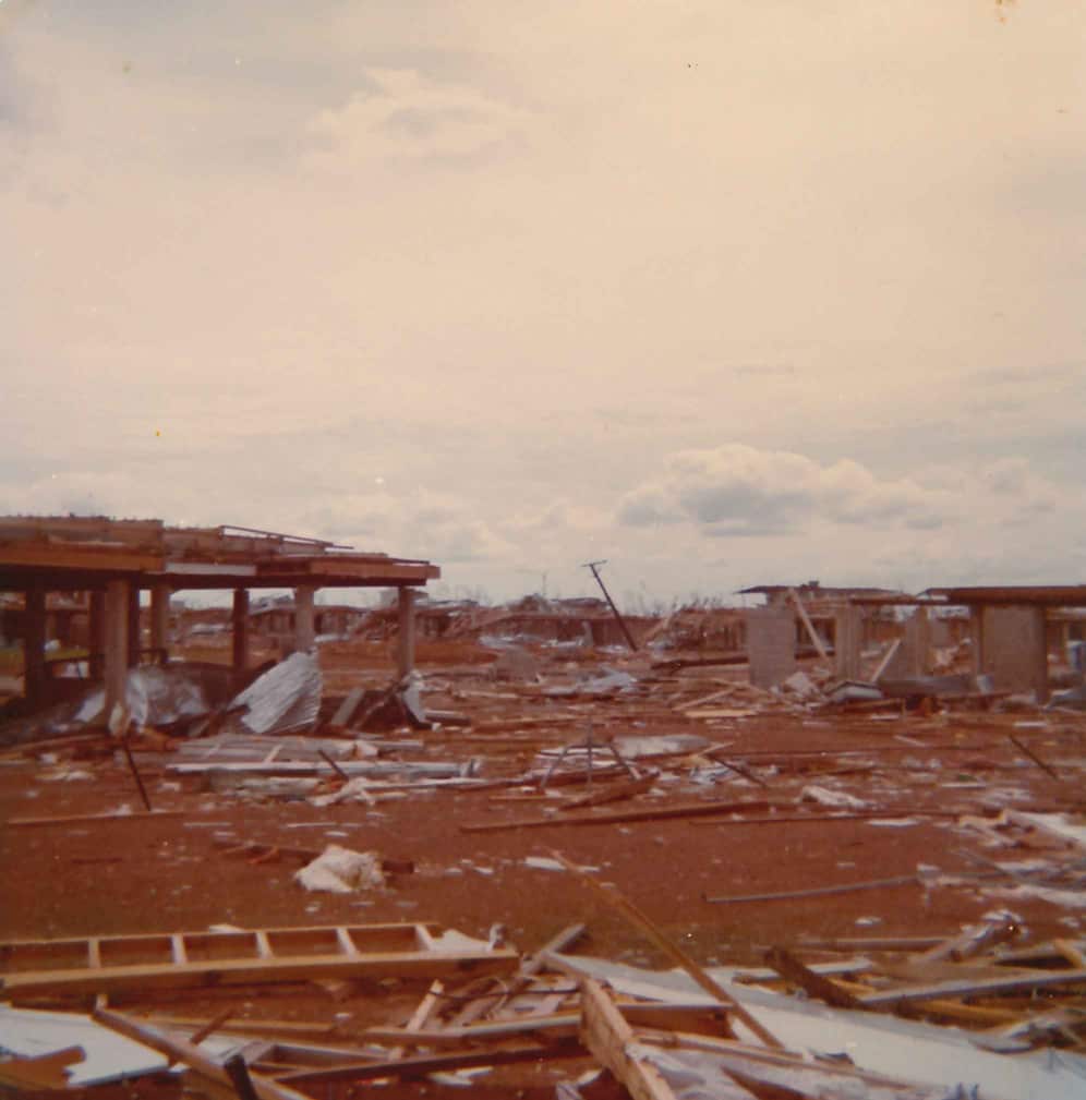 Debris scattered across red dirt, as parts of buildings stand destroyed.