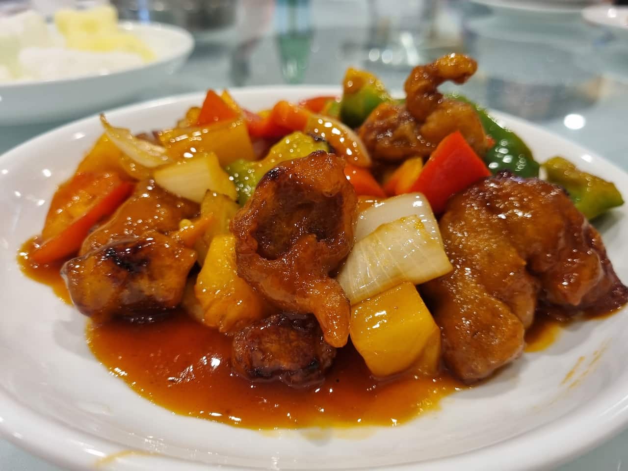 A dish of chopped up fried pork, capsicum, onion and pineapple covered in a red sauce