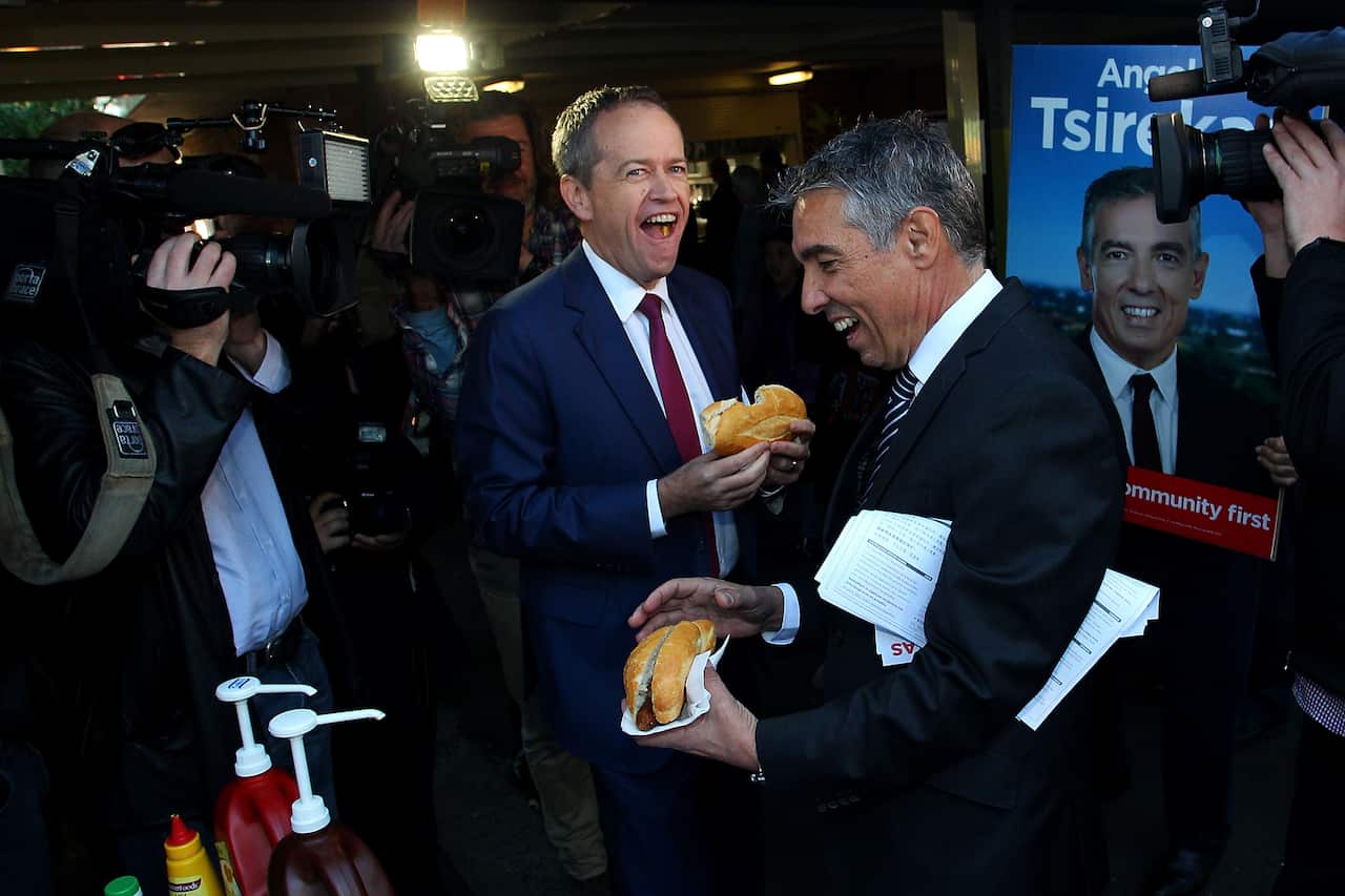 Man holds a sausage sizzle, smiling. 