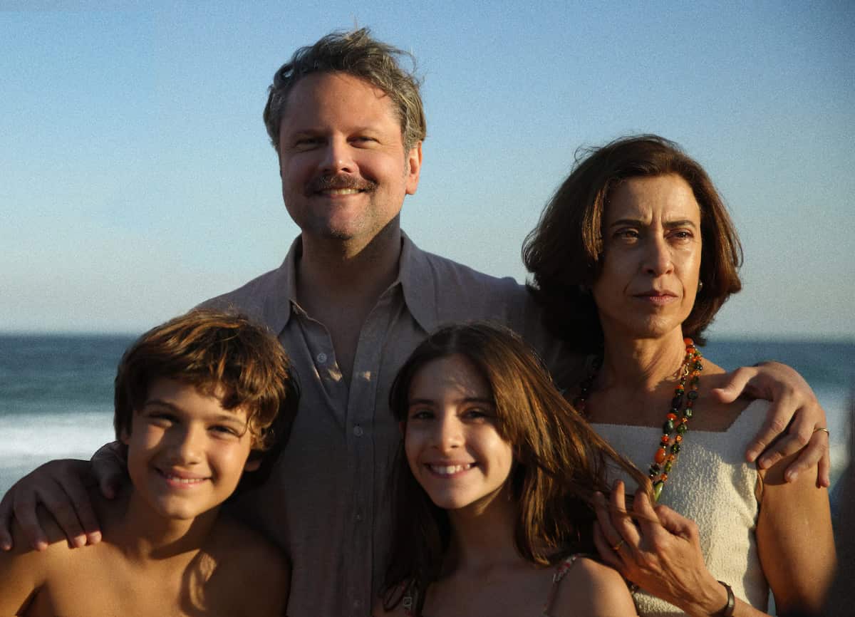 A couple and their two children, a boy and a girl, are smiling as they pose for the camera at a beach.