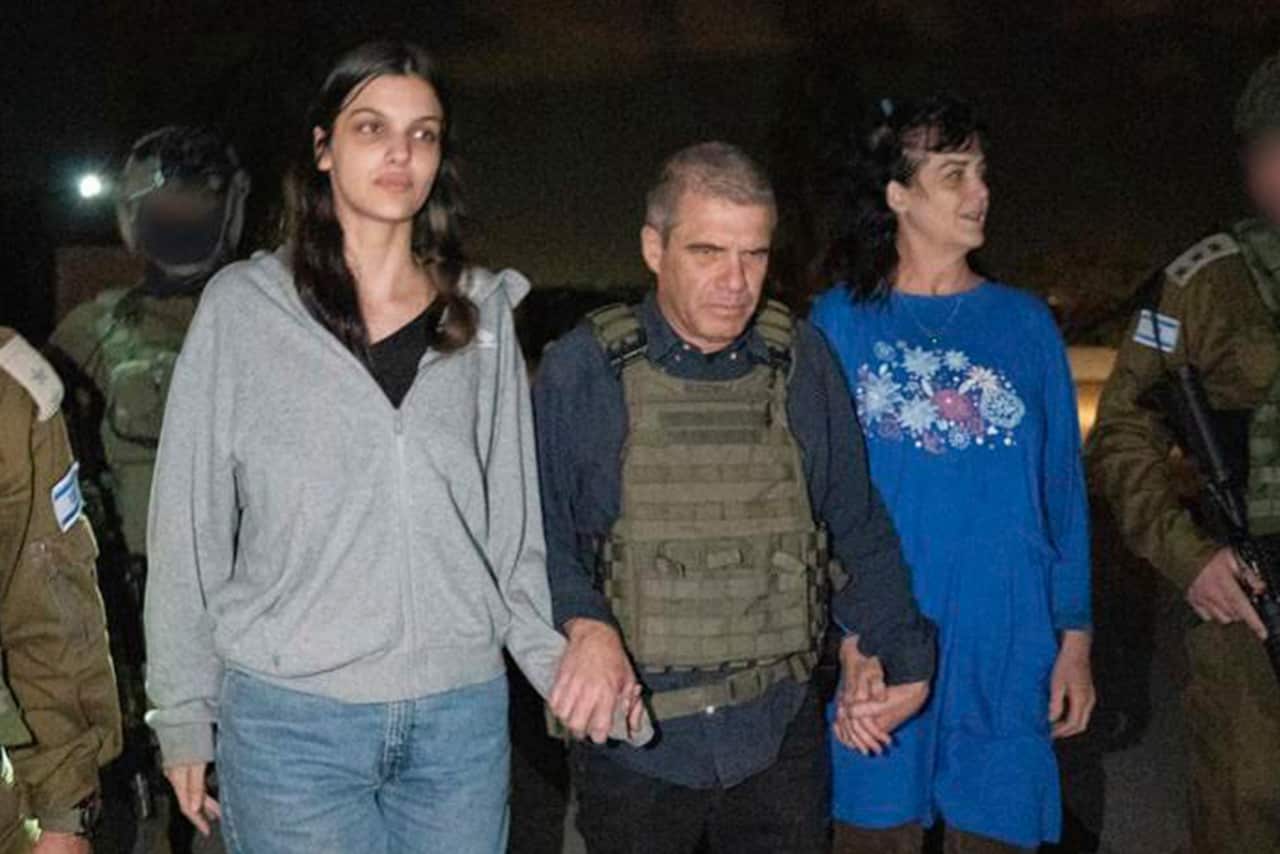 A man in a protective vest holds the hand of two women on either side of him.