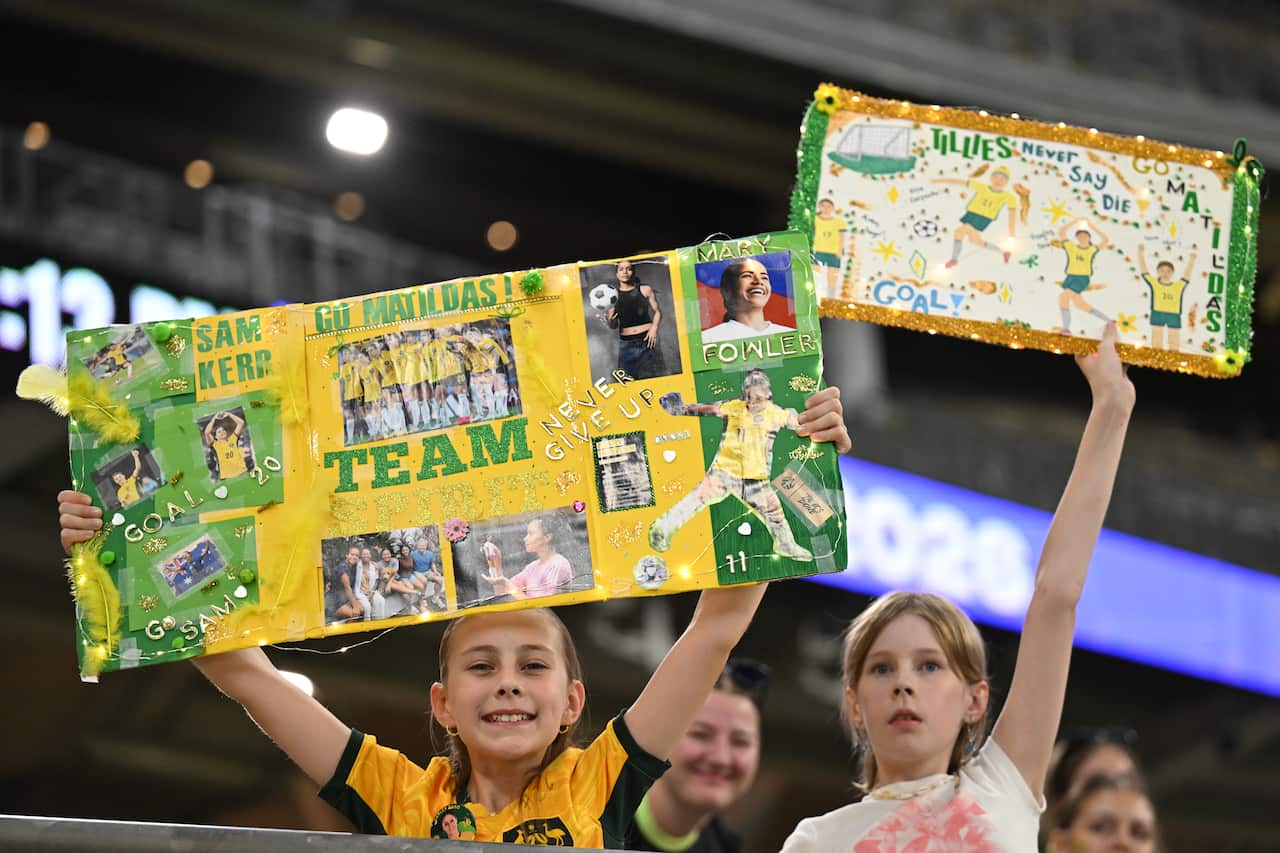 Two young girls hold placards saying Go Matildas and Tillies never say die as they watch the match between the Matildas and China in Perth 