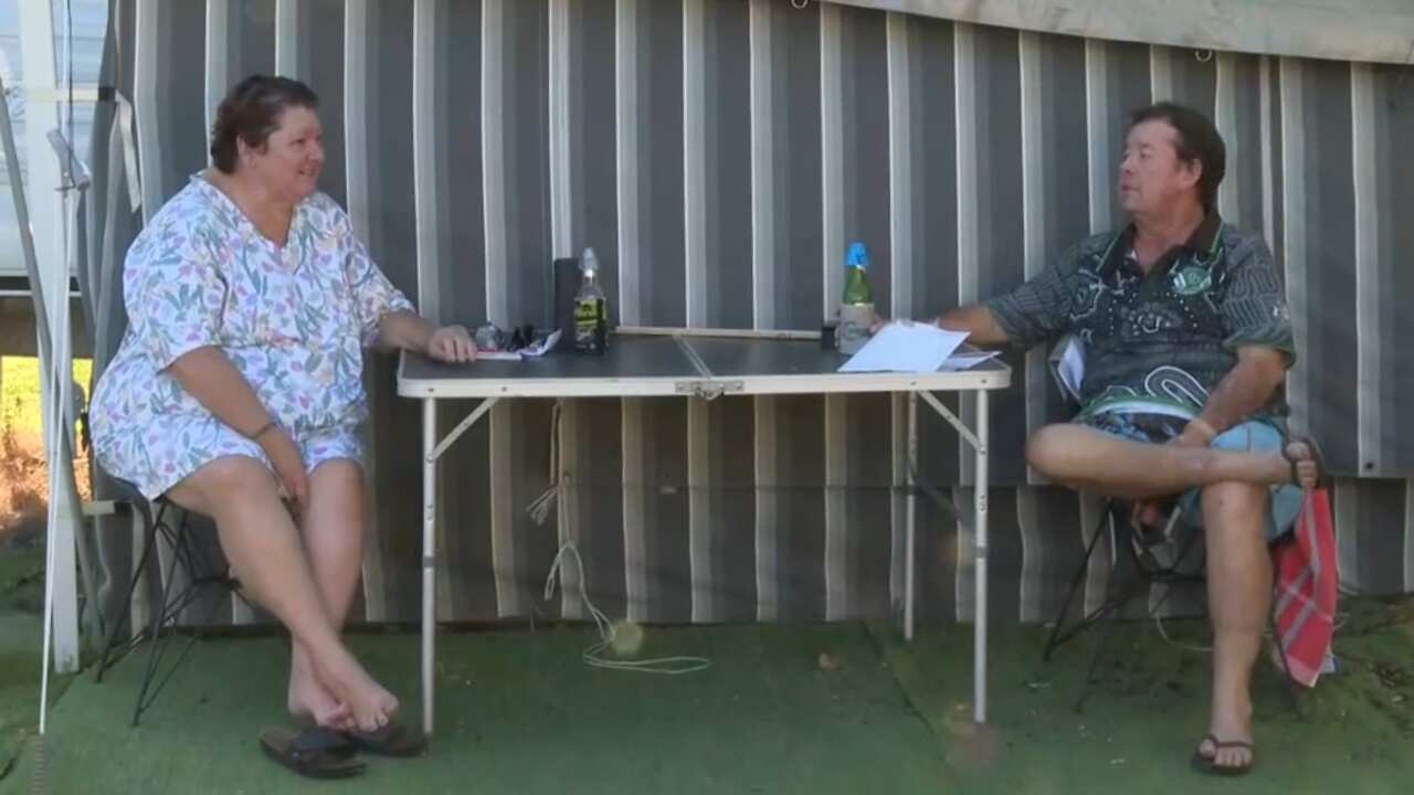 A woman and a man sit at a fold out table in front of a caravan awning.