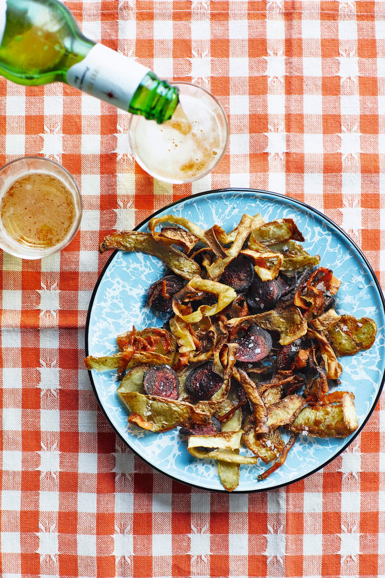 A plate of variously coloured vegetable crisps sit on a blue plate. 
