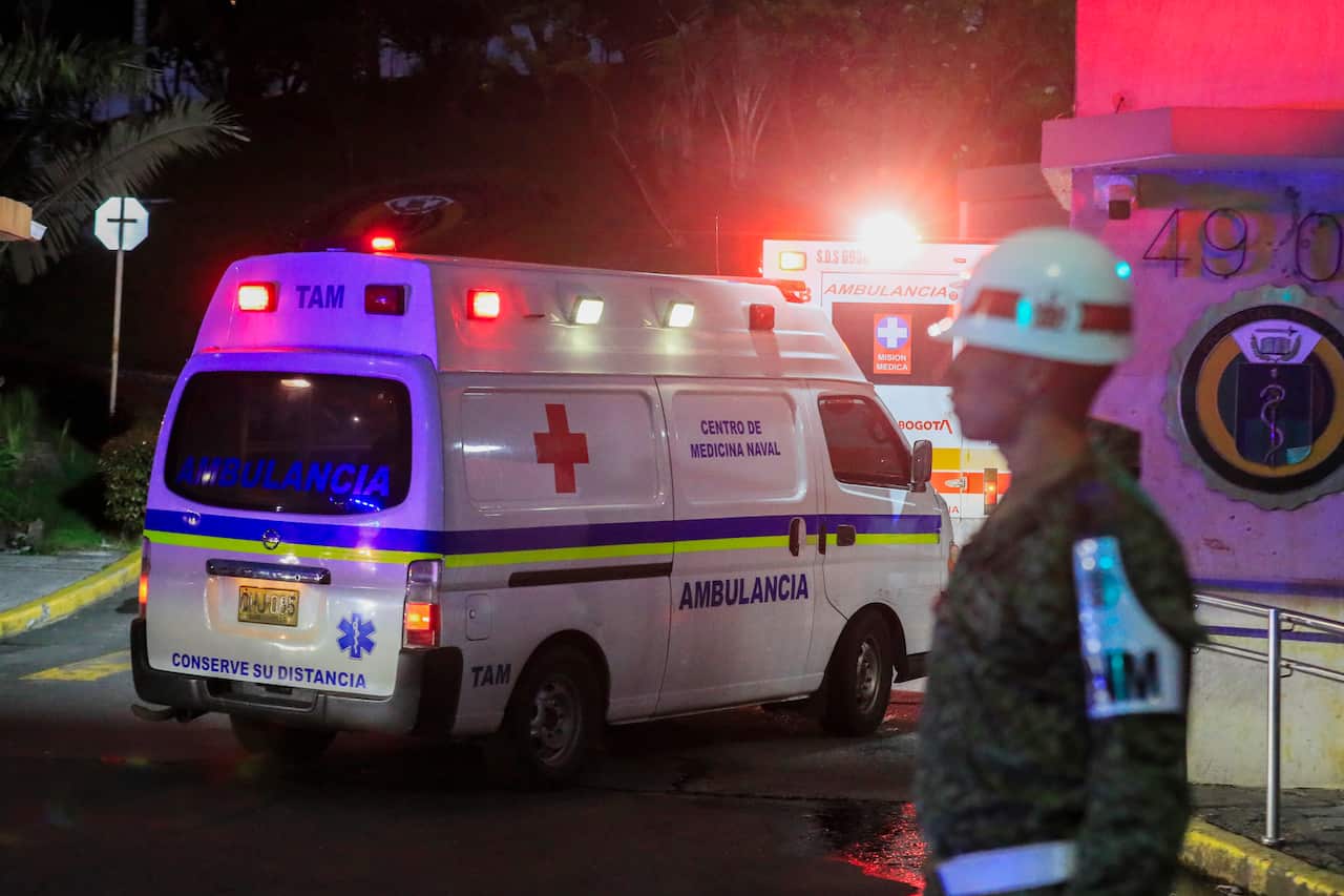 An ambulance driving away, as a man wearing military uniform stands nearby.