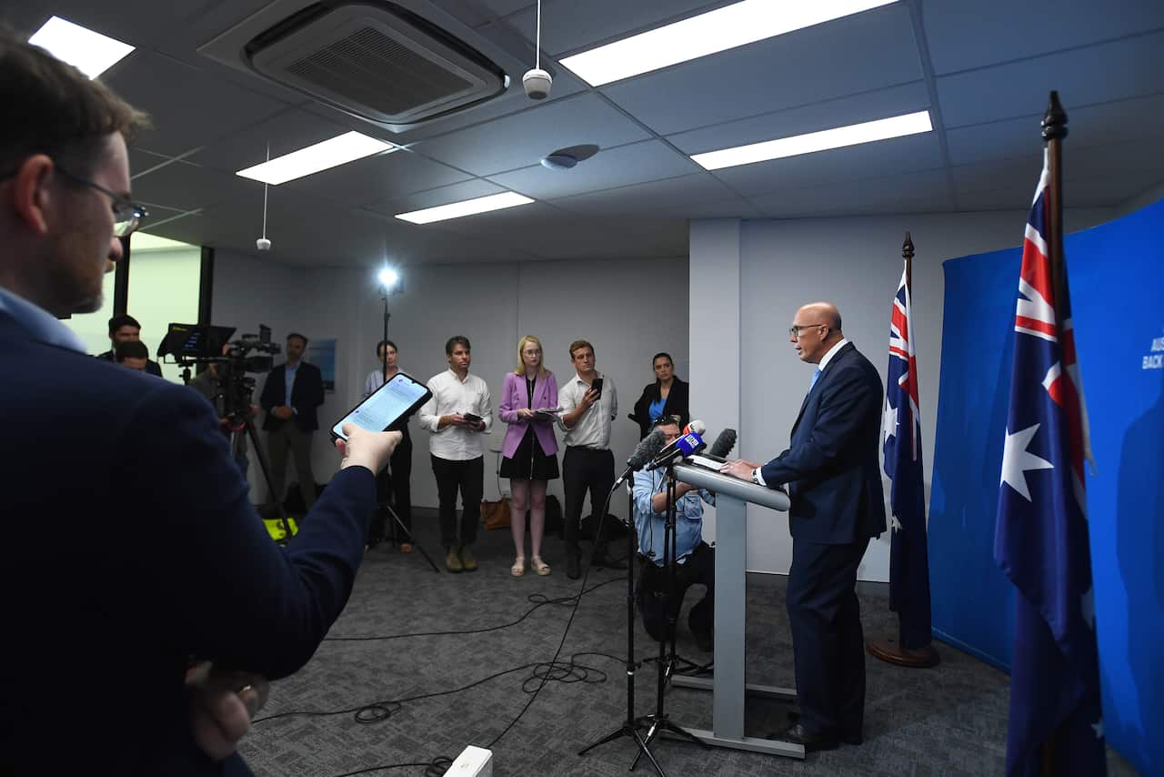 Peter Dutton speaks at a lectern as reporters watch on. 