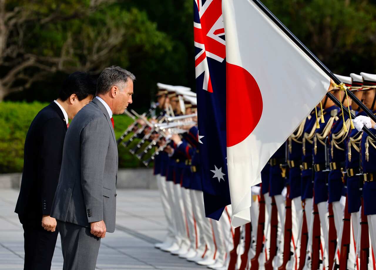 Two men bow in front of honour guards who are holding the Japanese and Australian flags.