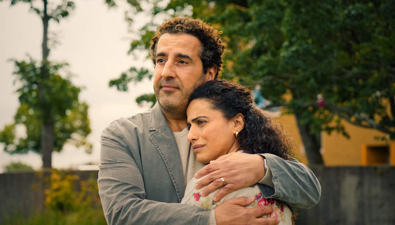 A man hugs a woman with a sad expression. 