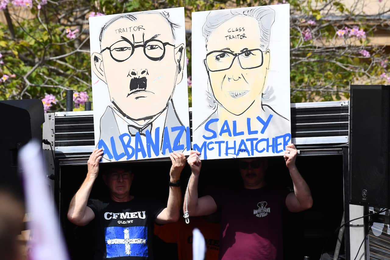 Two people holding placards. One on the left is a depiction of Anthony Albanese. The word "traitor" is written on his forehead, and "Albanazi" is written at the bottom of the poster. The other person is holding a placard of the Australian Council of Trade Unions secretary, Sally McManus. On her forehead, "class traitor" is written, and the bottom of the sign reads "Sally McThatcher".