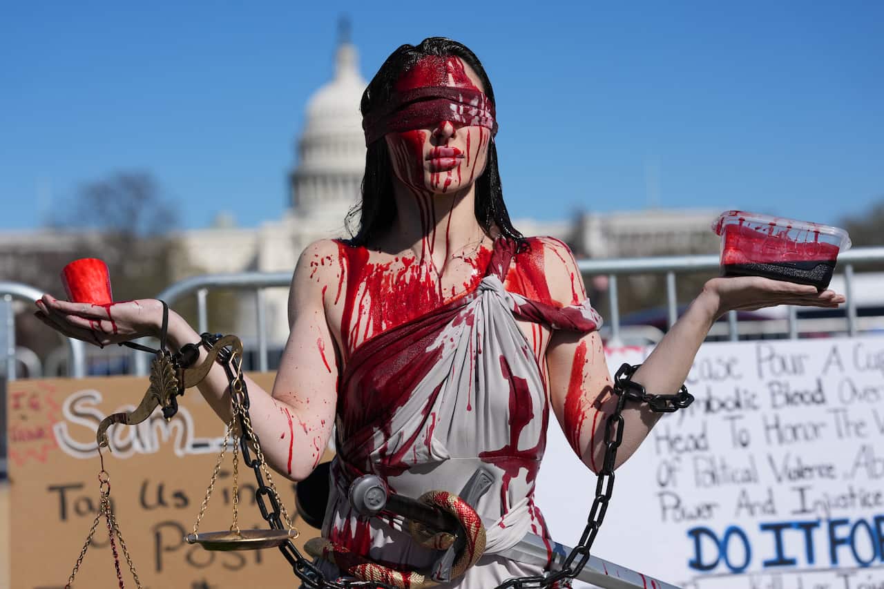 A woman dressed as Lady Justice is seen with fake blood on their face and body 
