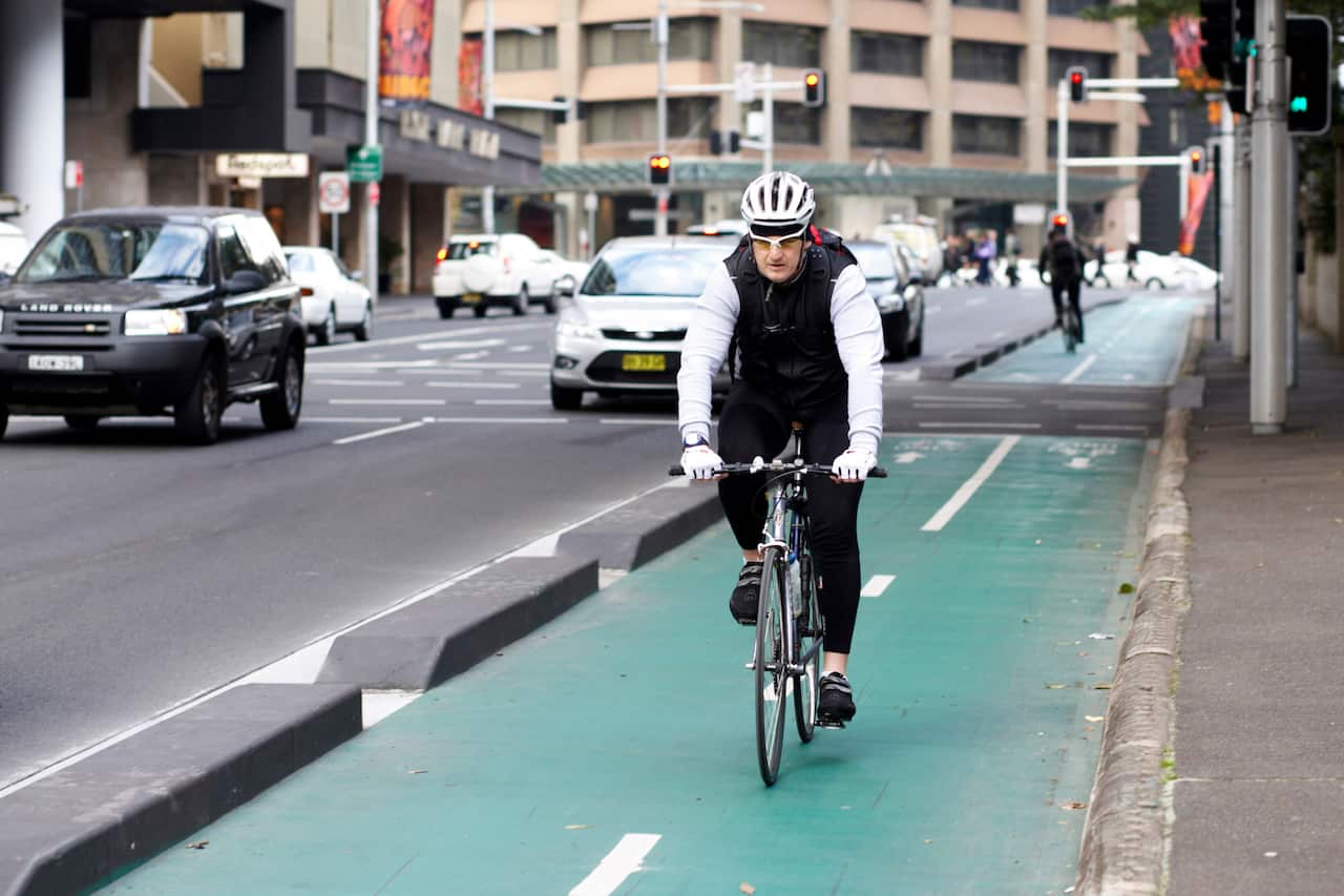 A man wearing a white helmet and a black vest cycles through the city in a bike lane.