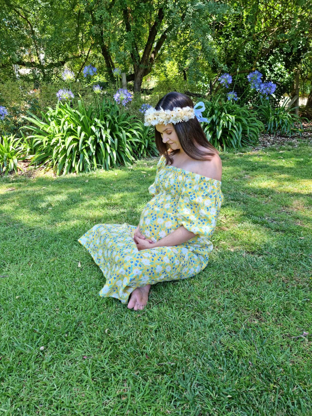 A pregnant woman sitting down on grass in a garden.