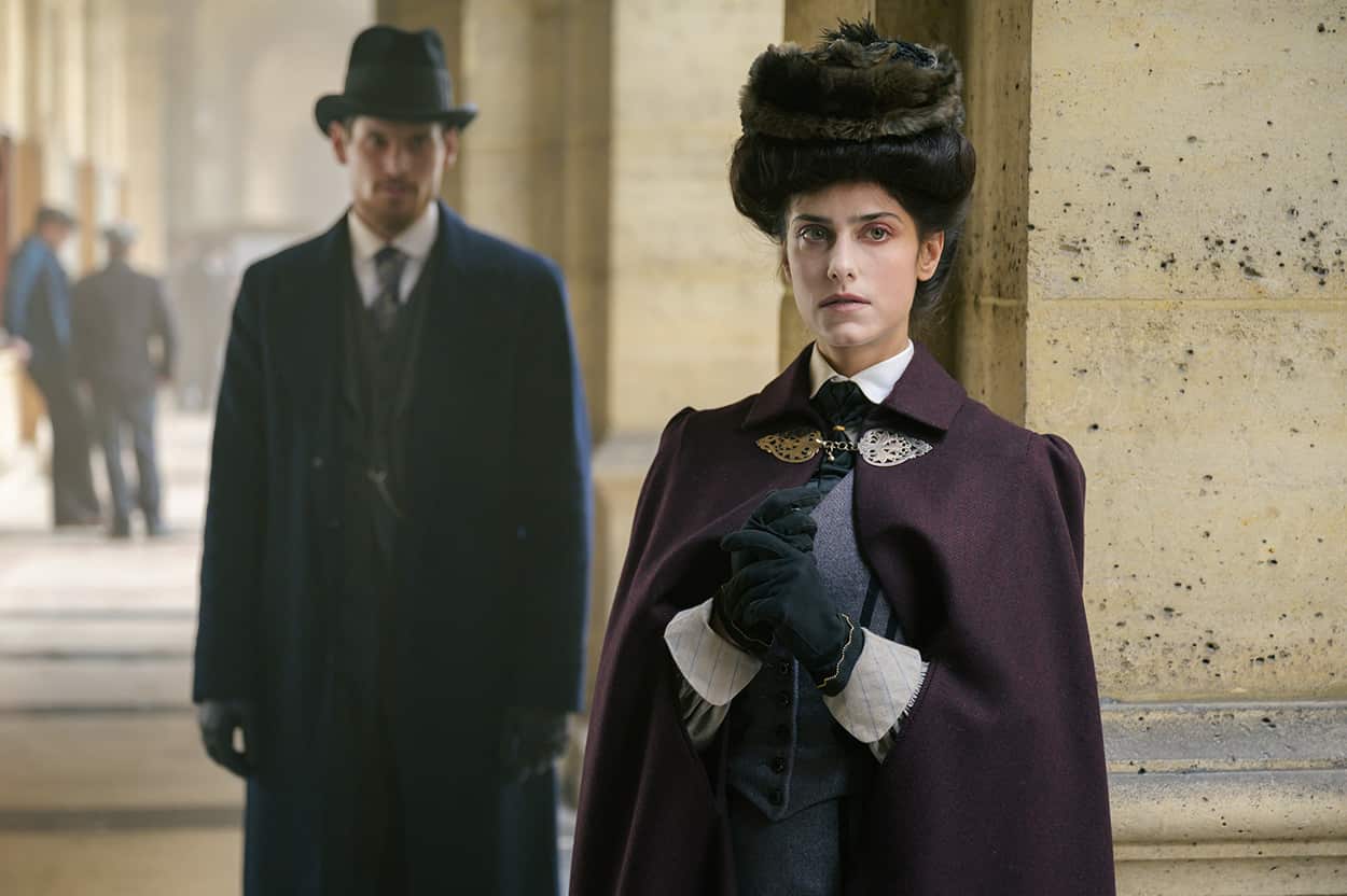 Woman in turn-of-the-century historical costume looks pensively ahead. 