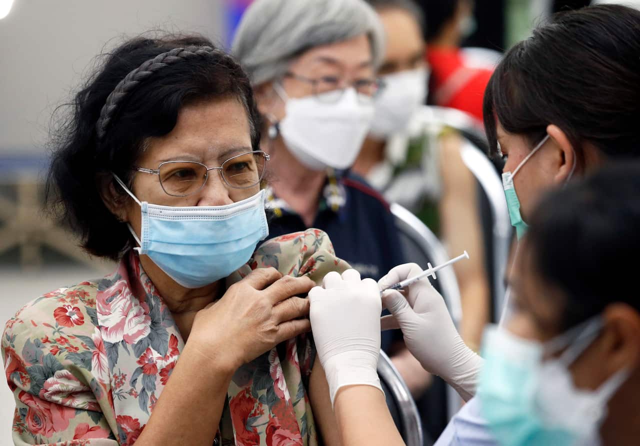 A middle-aged woman wearing glasses and a face mask receives a vaccine.