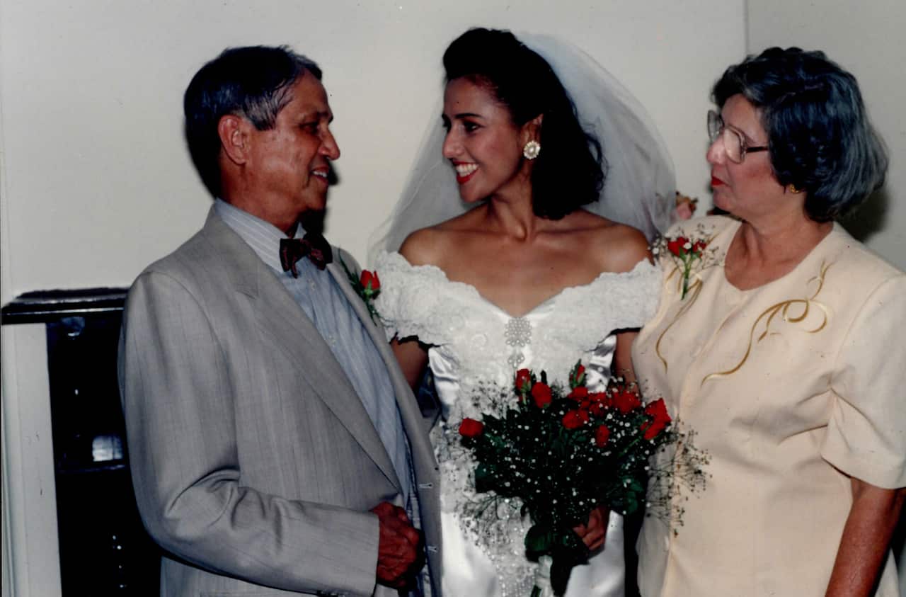 Alicia in a wedding dress smiling with her parents on her wedding day.